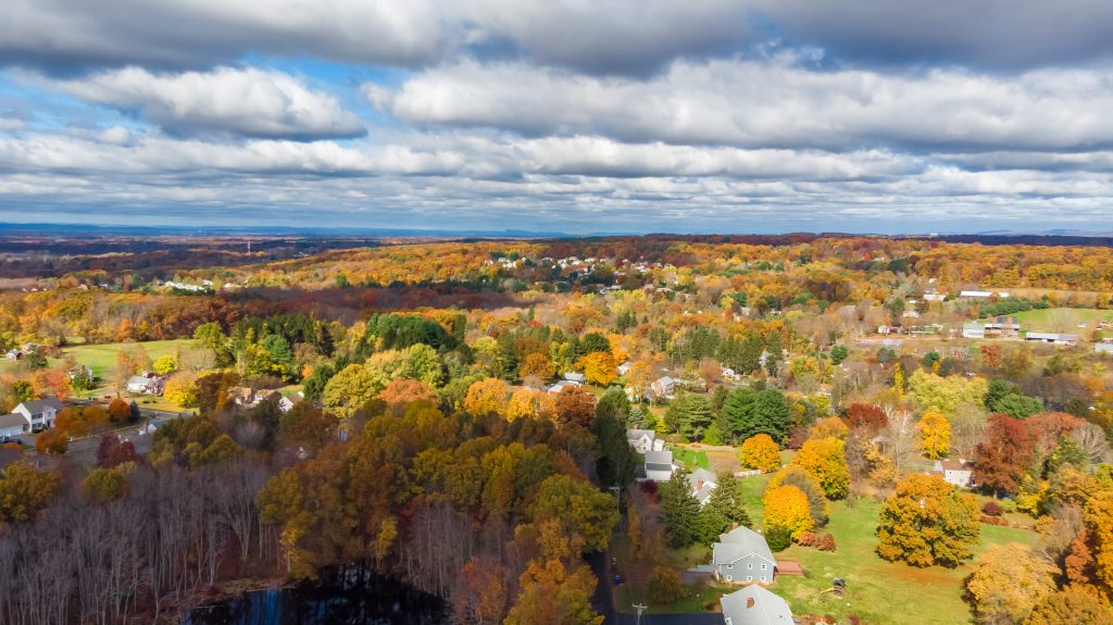 Aerial view of a suburban neighborhood surrounded by autumn foliage with scattered homes and tree-lined streets