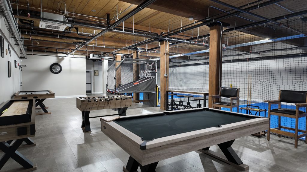 Game room at South Mill Lofts with pool table, foosball, shuffleboard, and basketball arcade under exposed wood beams
